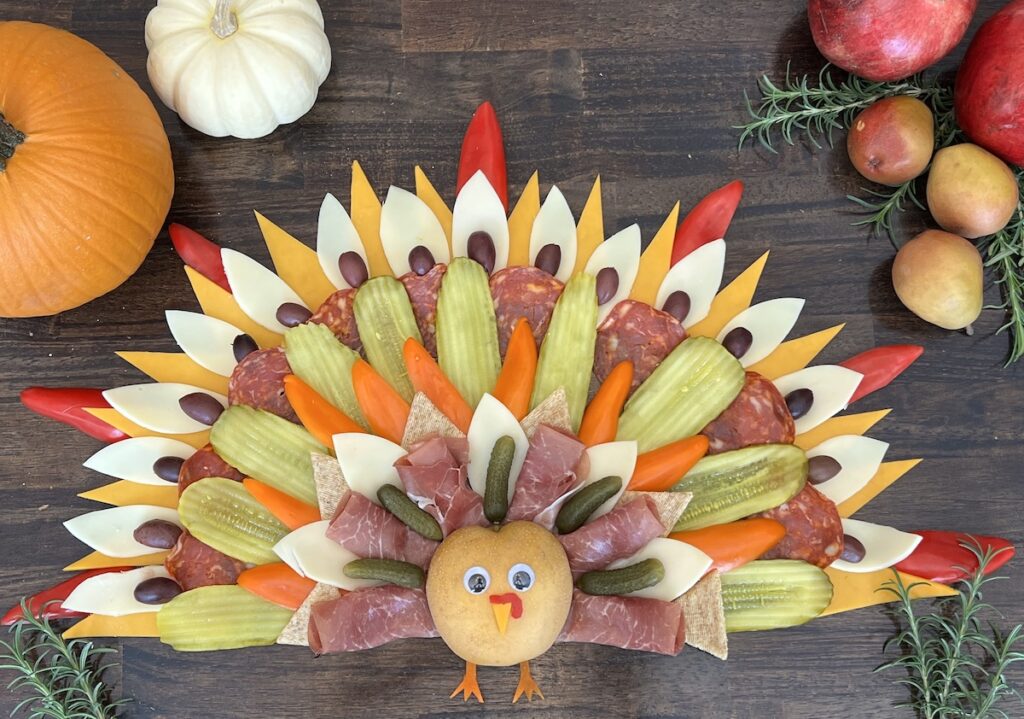 sliced meats, cheeses, peppers, olives arranged on a board to look like a Thanksgiving turkey