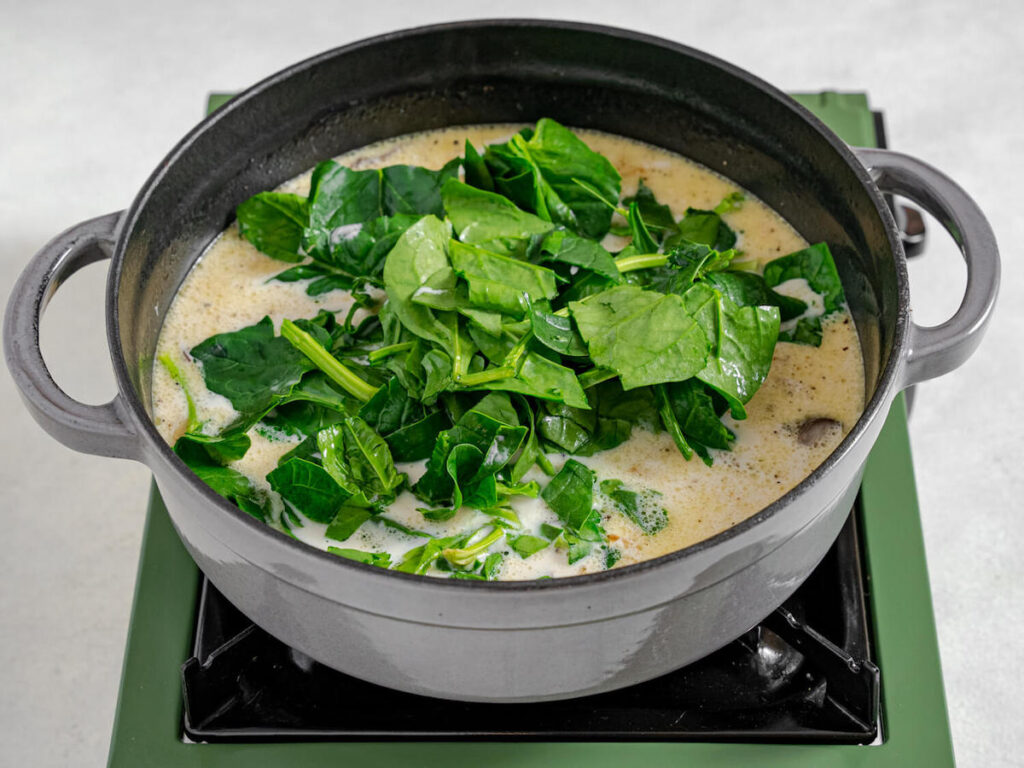 baby spinach added to creamy hearty winter soup from Flavor Portal recipe simmering in a pot