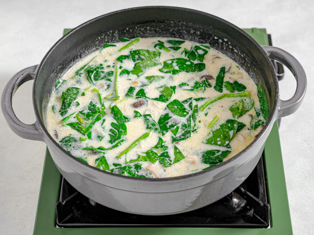 baby spinach stirred into creamy hearty winter soup from Flavor Portal recipe simmering in a pot