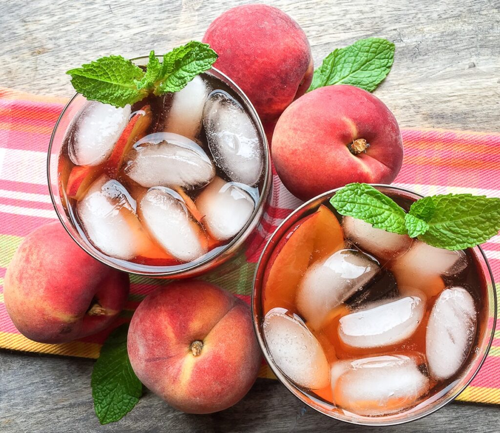 Instant Pot Ginger Peach Iced Tea from Flavor Portal recipe in two glasses with a mint sprig next to peaches and mint leaves