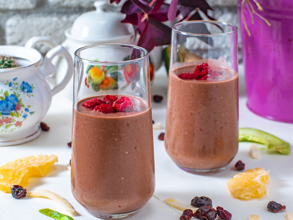 two tall glasses of keto chocolate raspberry smoothies from Flavor Portal recipe garnished with fresh raspberries
