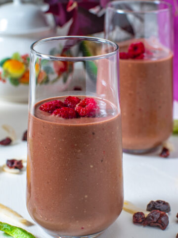 two tall glasses of keto chocolate raspberry smoothies from Flavor Portal recipe garnished with fresh raspberries