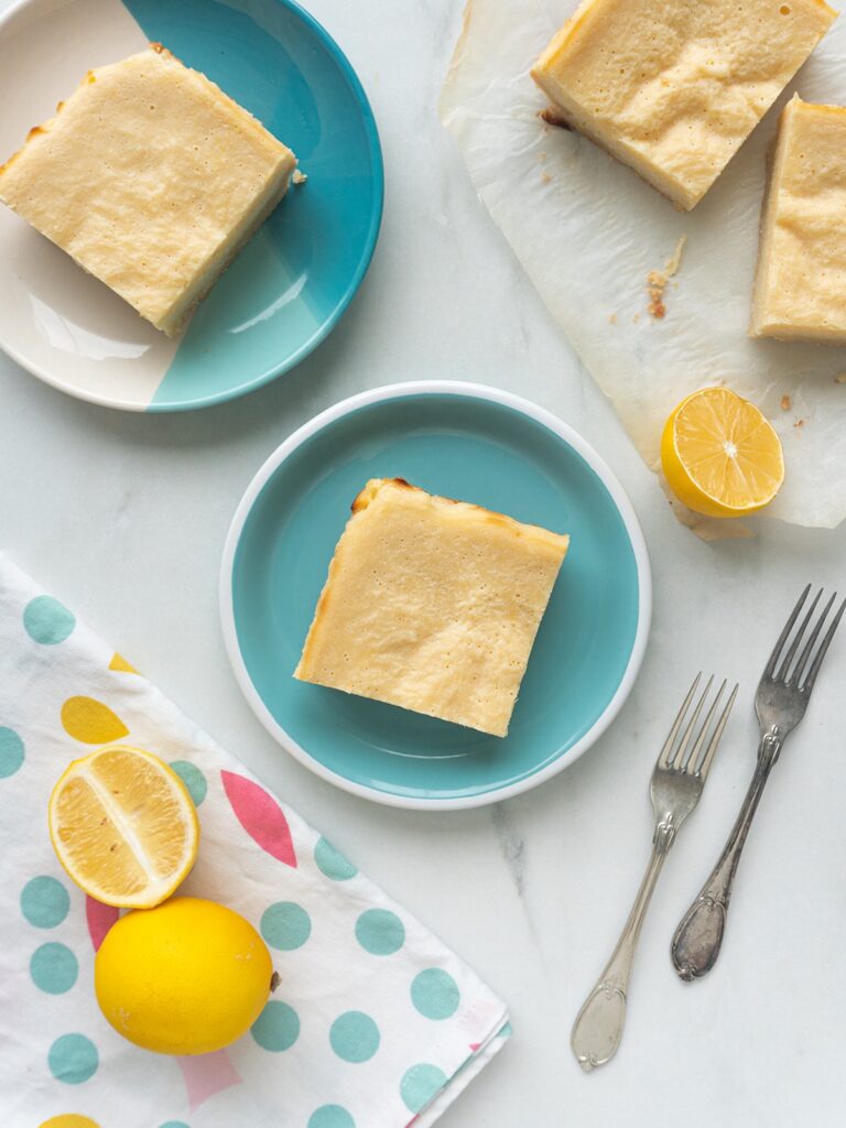 keto lemon bar from Flavor Portal recipe on a light blue plate next to lemon wedges and a little stack of keto lemon bars