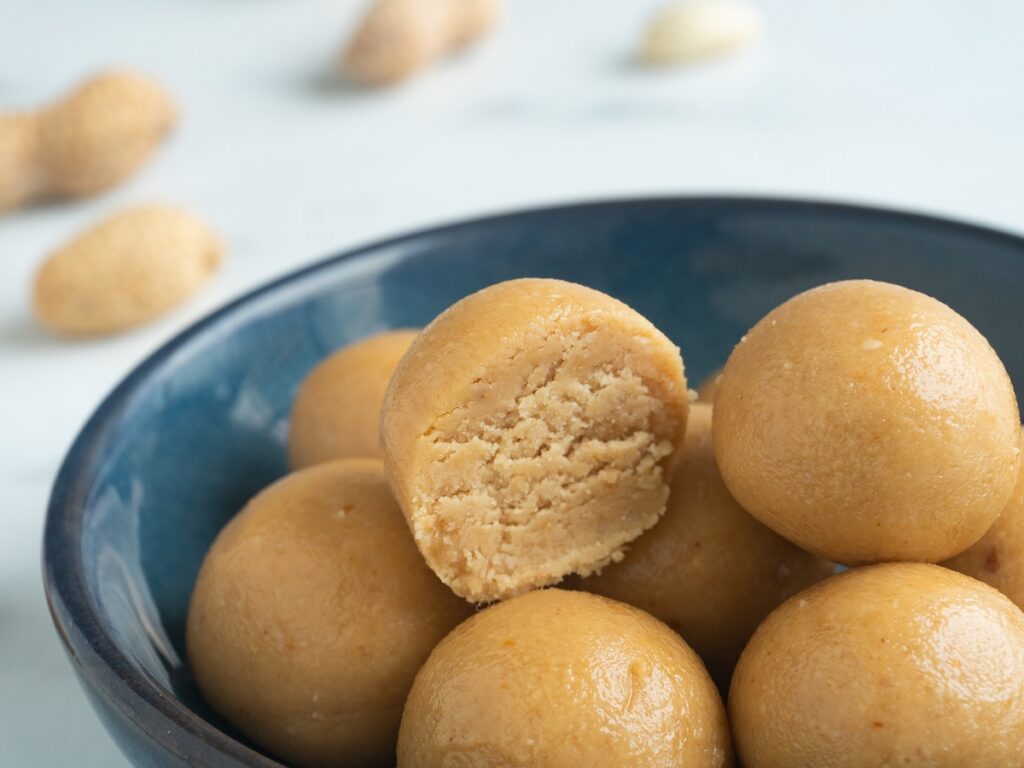 keto peanut butter balls from Flavor Portal recipe in a blue bowl with scattered peanuts next to it