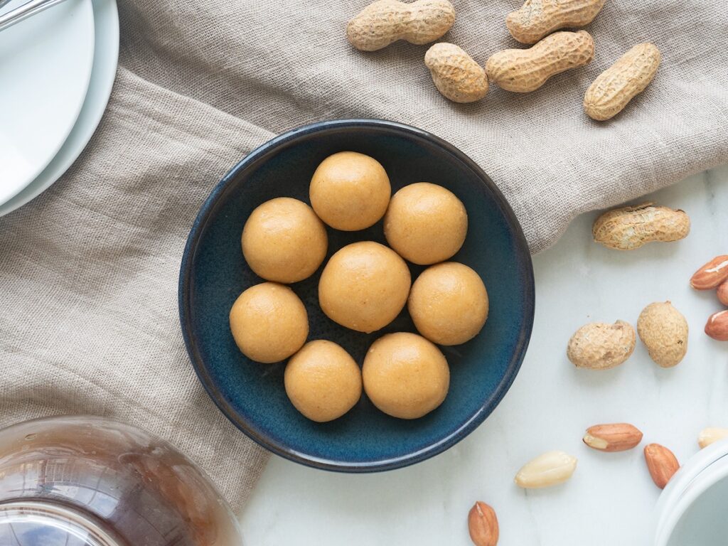keto peanut butter balls from Flavor Portal recipe in a blue bowl with scattered peanuts next to it