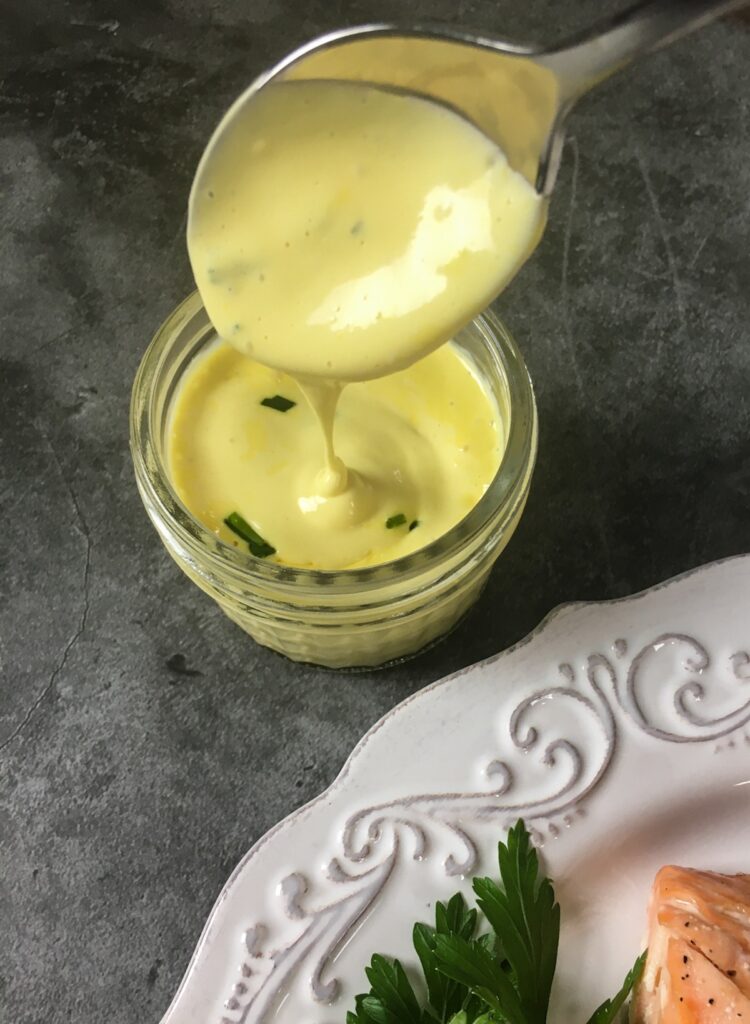 keto salmon with hollandaise sauce from Flavor Portal recipe on a white plate with steamed broccoli, cherry tomatoes and a parsley garnish with hollandaise sauce on the side