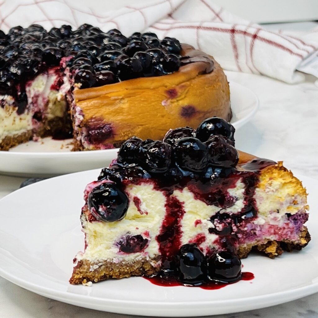 slice of keto blueberry jamboree cheesecake from Flavor Portal recipe in front of the keto blueberry jamboree cheesecake
