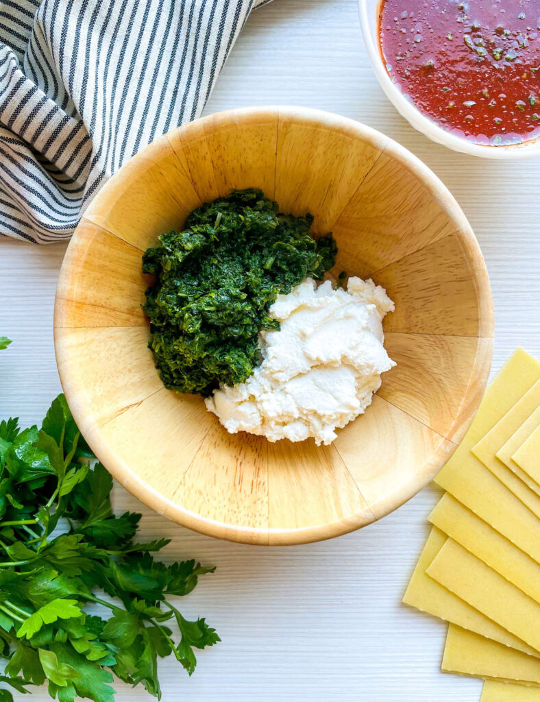 spinach and ricotta in a wooden bowl surrounded by parsley, pasta and tomato sauce for Spinach and Ricotta Lasagna Roll Ups from Flavor Portal recipe
