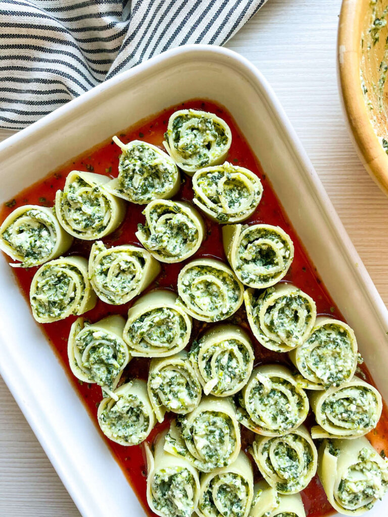 uncooked spinach and ricotta lasagna rollups on tomato sauce in a baking pan for Spinach and Ricotta Lasagna Roll Ups from Flavor Portal recipe