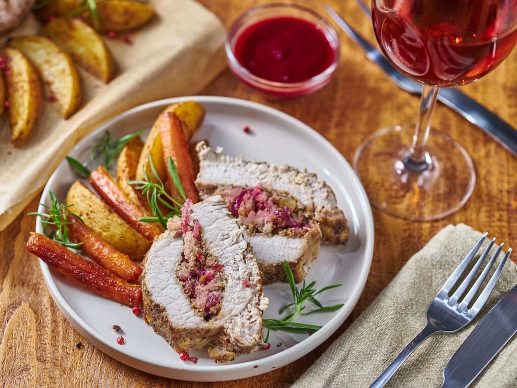 Apple and Walnut Stuffed Pork Tenderloin from Flavor Portal recipe on a cutting board with potato wedges and a glass of wine