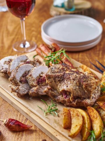 Apple and Walnut Stuffed Pork Tenderloin from Flavor Portal recipe on a cutting board with potato wedges and a glass of wine