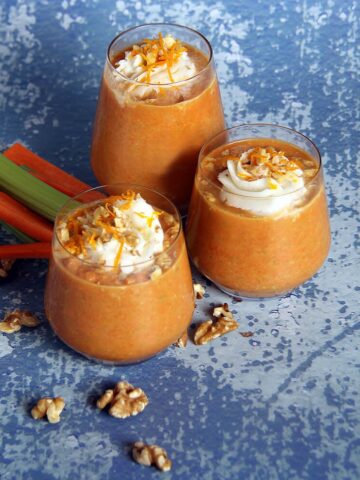 three glasses of carrot cake smoothie from Flavor Portal recipe with scattered walnut pieces, carrot and celery sticks