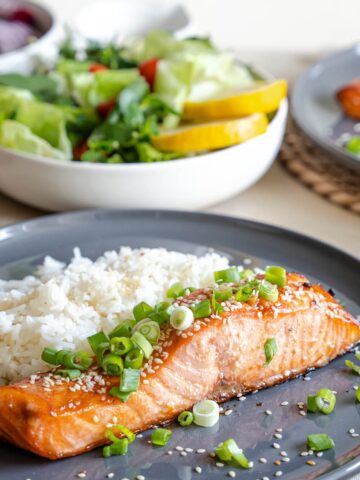 hot honey sriracha salmon from Flavor Portal recipe garnished with sliced green onions with rice and a bowl of mixed green salad