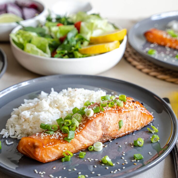 hot honey sriracha salmon from Flavor Portal recipe garnished with sliced green onions with rice and a bowl of mixed green salad