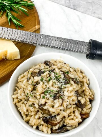 rustic mushroom risotto from Flavor Portal recipe in a white bowl beside a cutting board with cheese and a cheese grater