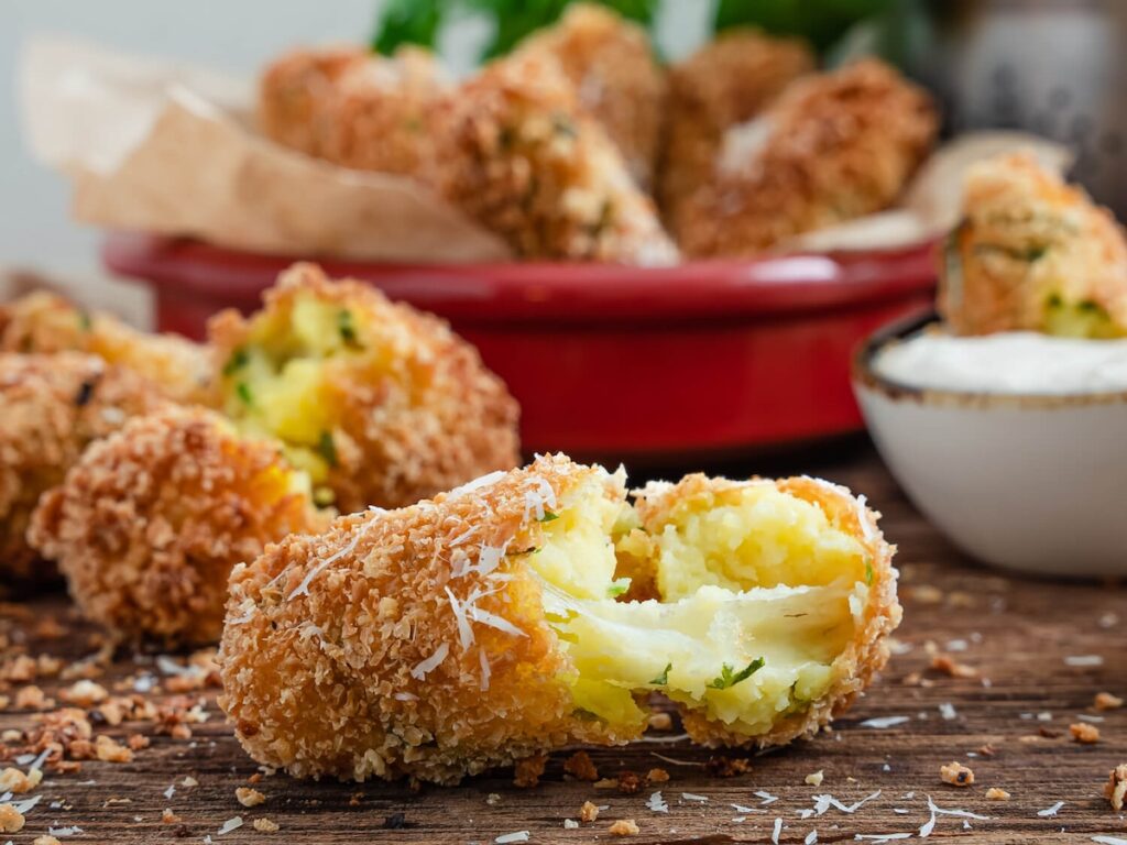 cheese stuffed mozzarella potato croquettes from Flavor Portal recipe in a bowl behind one broken open to show the melted cheese inside