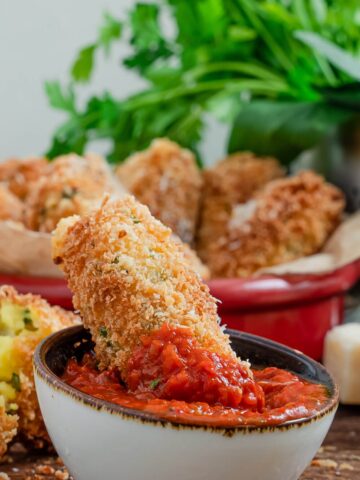 cheese stuffed mozzarella potato croquettes from Flavor Portal recipe in a bowl behind one dipped in marinara sauce