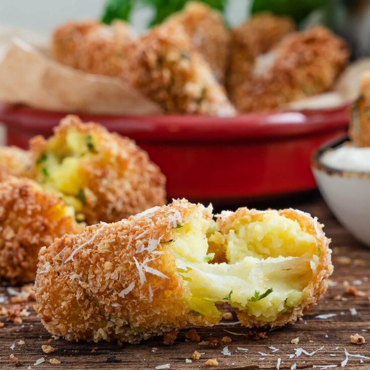 cheese stuffed mozzarella potato croquettes from Flavor Portal recipe in a bowl behind one broken open to show the melted cheese inside