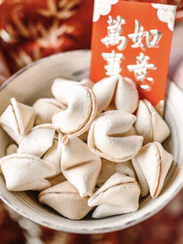 bowl of fortune cookies with a red card that has gold Chinese writing on it