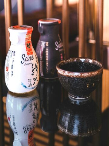 A small bottle of sake next to a traditional sake cup.